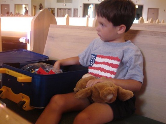 Young boy with teddy bear and suitcase at Church pew