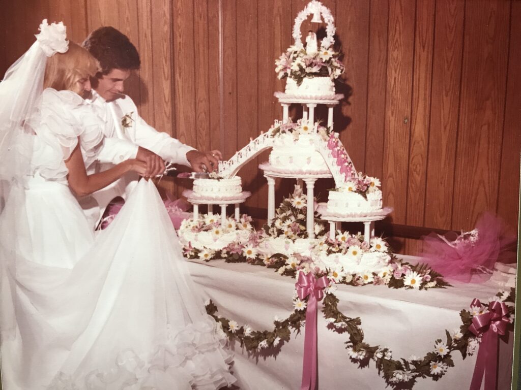 newly married couple posing for pictures while cutting wedding cake