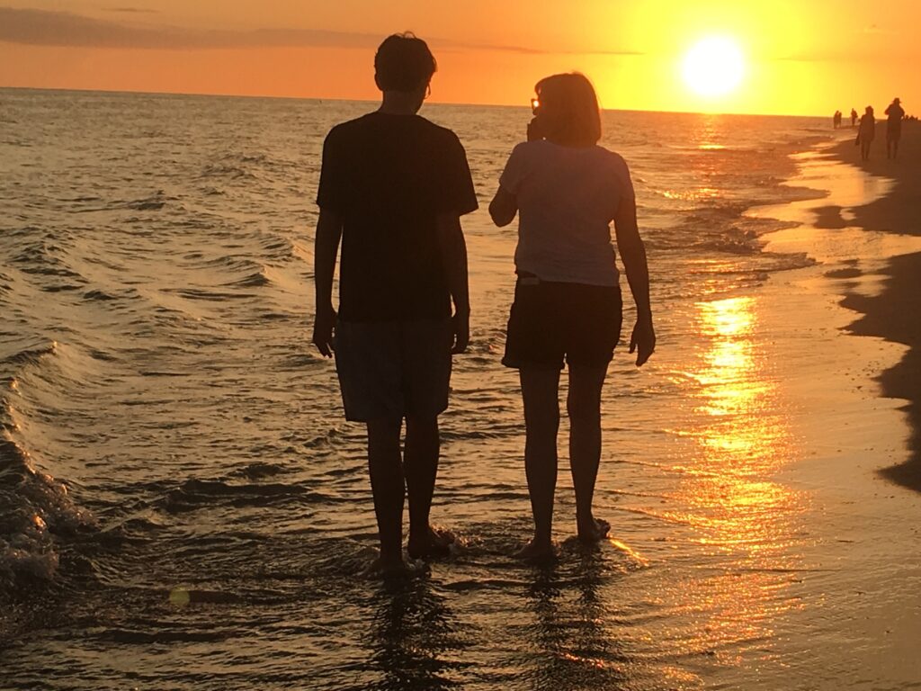 Two people walking on the beach at sunset