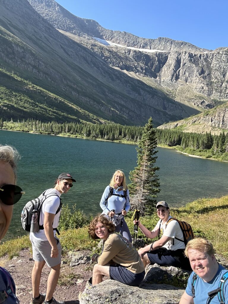 six hikers sitting next to mountain lake